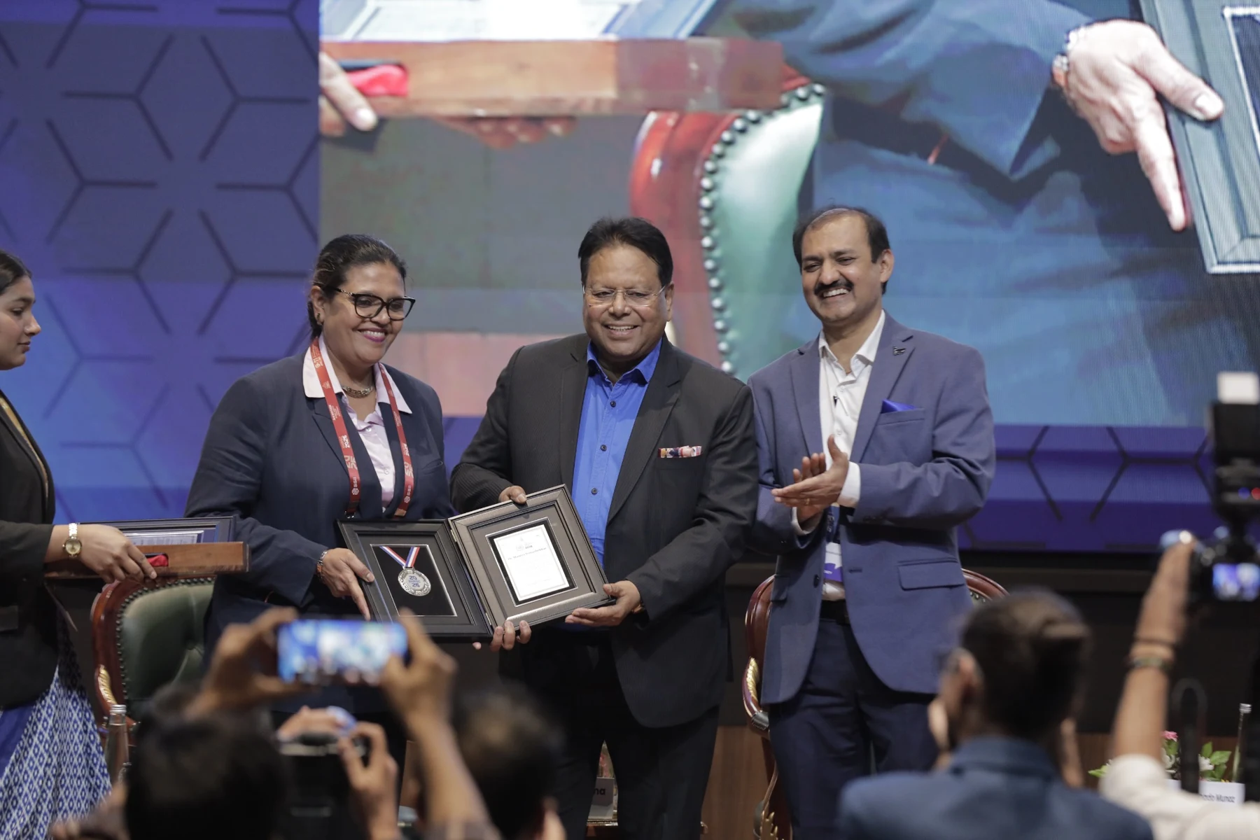 Three participants on stage with a framed presentation
