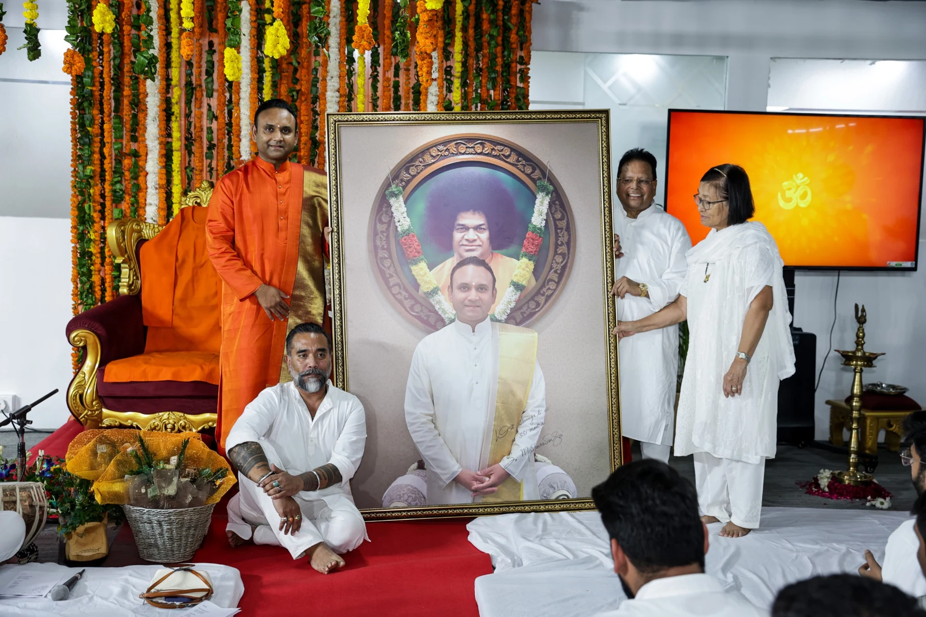 A ceremonial gathering with participants, floral decorations and a framed portrait